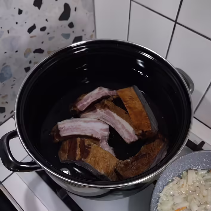 ребра в каструлі. Праворуч - готується піджарка з цибулі та моркви